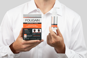 一名男性手持含5%米諾地爾和5% TRIOXIDIL的FOLIGAIN外用護理產品包裝盒與噴霧瓶。
