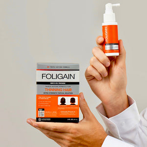 雙手拿著FOLIGAIN男用10% TRIOXIDIL外用護理產品的包裝盒與噴霧瓶。